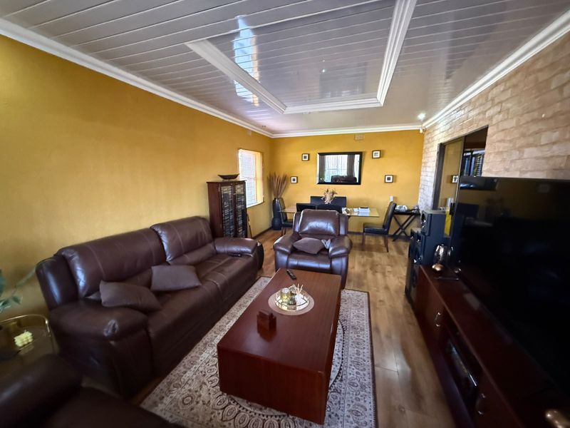 A living room featuring laminate flooring, an exposed brick feature wall, and a recessed ceiling panel with coved cornice detailing.