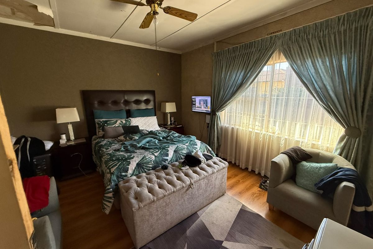A bedroom featuring laminate flooring and a ceiling fan, currently showing signs of ceiling damage and wear requiring maintenance.