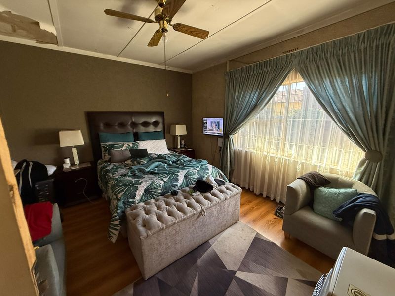 A bedroom featuring laminate flooring and a ceiling fan, currently showing signs of ceiling damage and wear requiring maintenance.