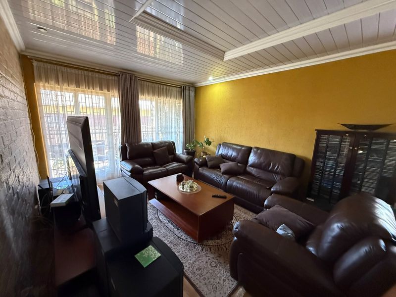 A living room featuring an exposed brick wall, tongue and groove ceiling, and sliding glass doors with security bars leading to an outdoor area.