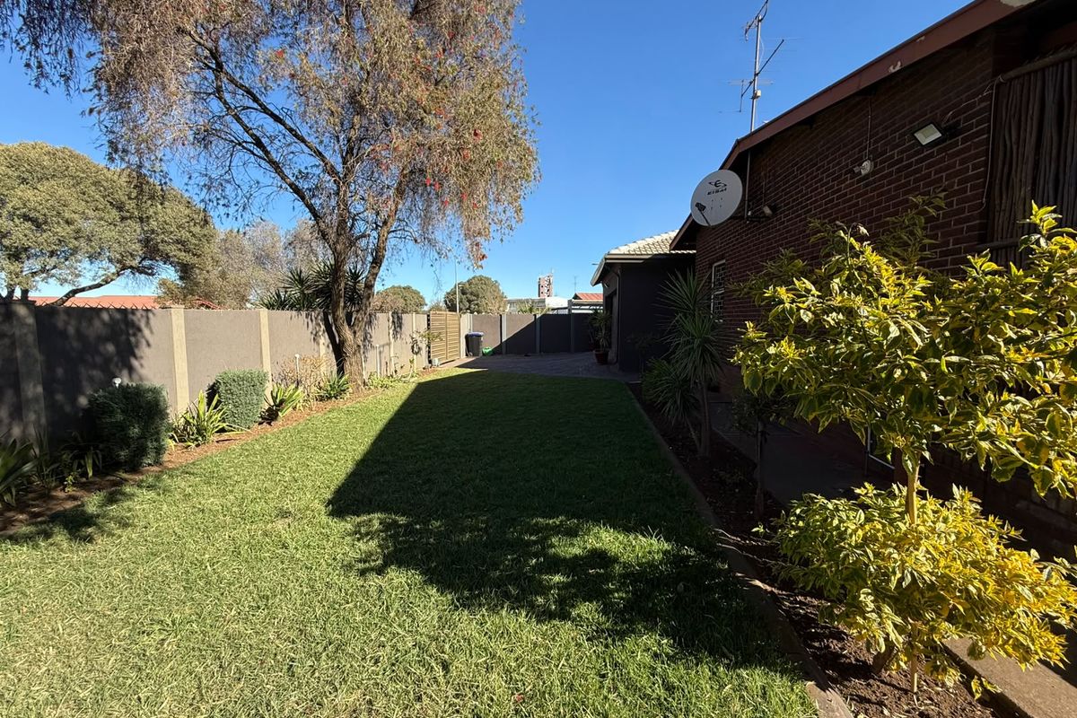 A well-maintained rear garden featuring a lush green lawn, brick boundary walls, and established landscaping along the side of the house.