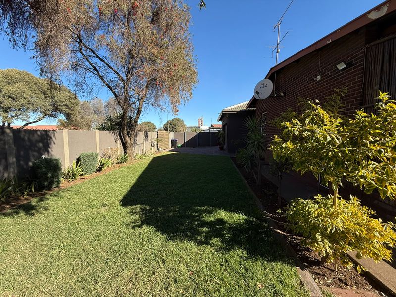 A well-maintained rear garden featuring a lush green lawn, brick boundary walls, and established landscaping along the side of the house.