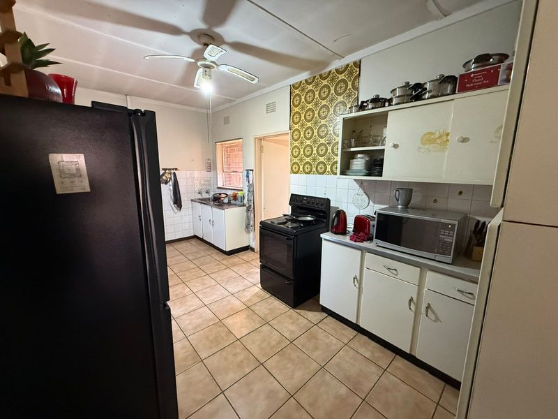 A functional kitchen featuring tiled flooring, built-in cabinetry, a freestanding stove, and a tiled backsplash, offering potential for modernization and cosmetic updates.