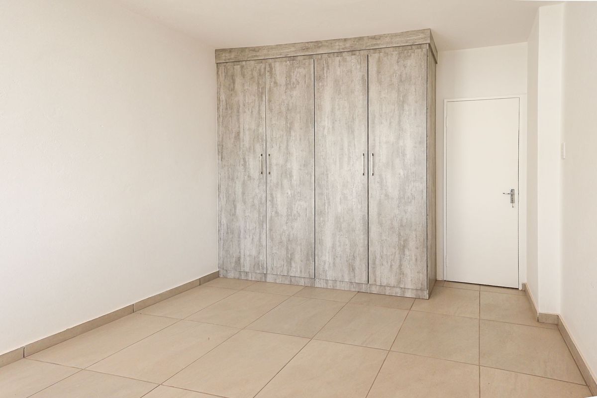 A clean, empty bedroom featuring neutral tiled flooring and modern wood-look built-in cupboards, providing a versatile space ready for furnishing.