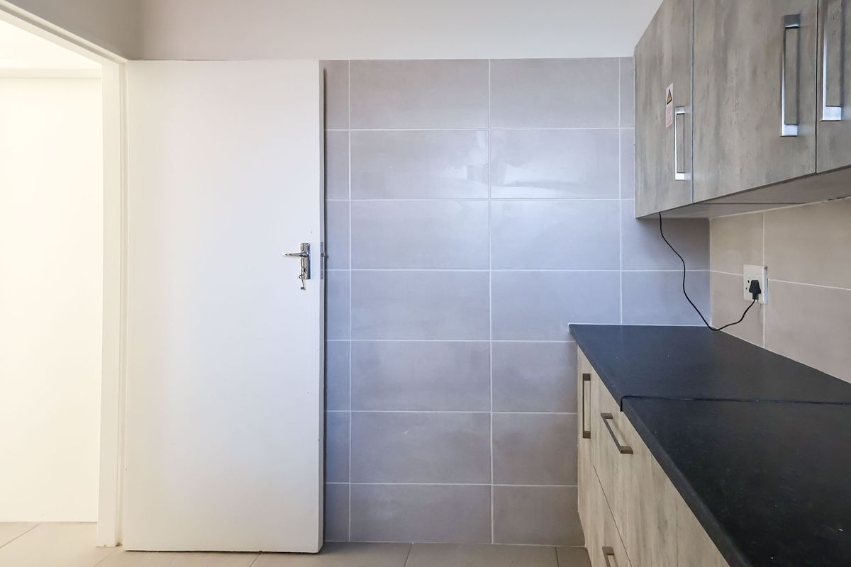 A clean, modern kitchen area featuring grey laminate cabinetry, a black countertop, and neutral tiled splashback, presenting a functional and well-maintained space.