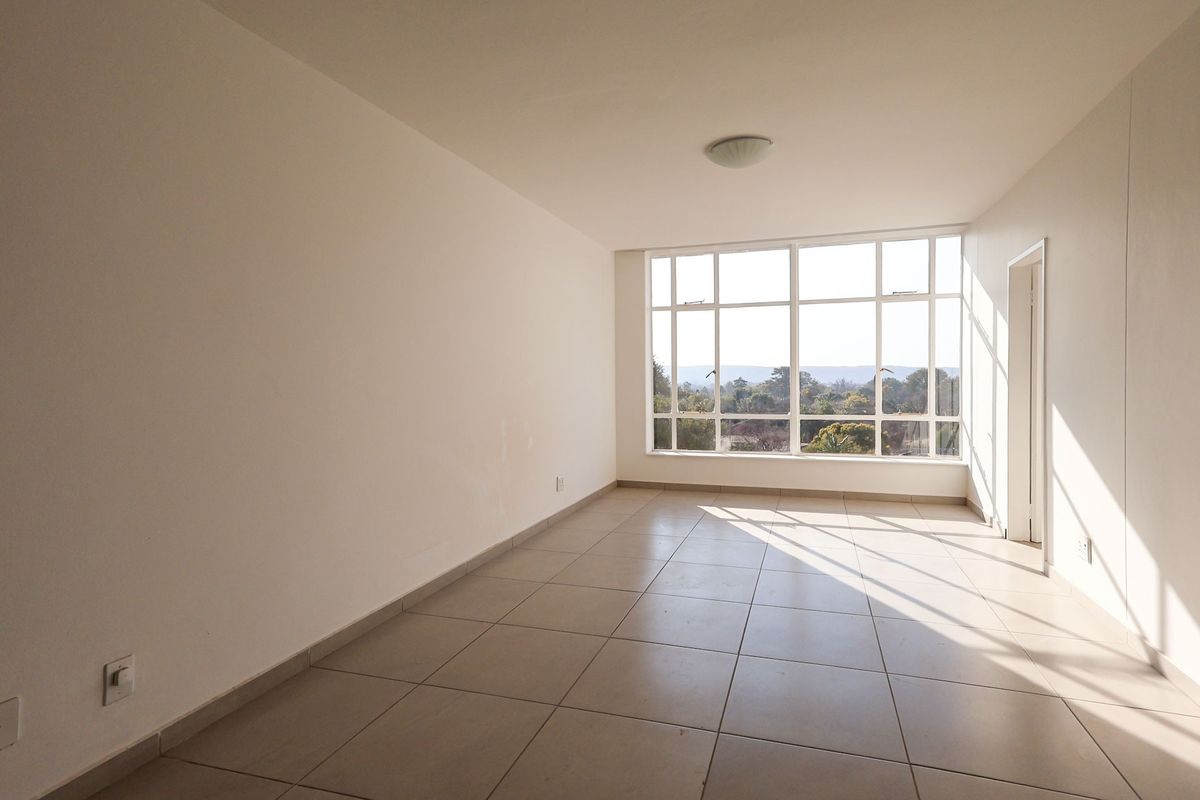 A bright, empty living room featuring large windows with natural light, tiled flooring, and neutral walls, offering a blank canvas for interior design.