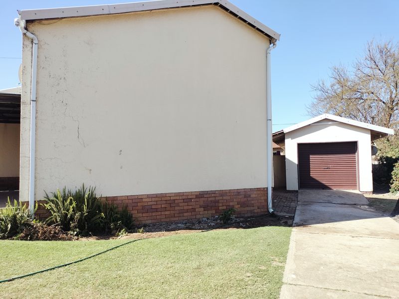 Rear exterior view showing a detached garage, concrete driveway, and the side elevation of the main dwelling with visible brick plinth and wall cracks.