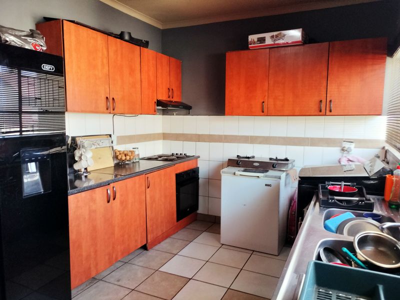 A functional kitchen featuring wood-look cabinetry, tiled backsplash, and integrated cooking appliances, offering a practical layout with ample storage space.
