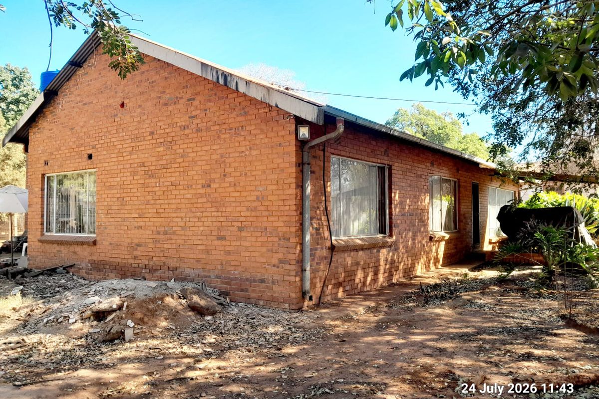 Rear view of a single-story brick farmhouse featuring exposed masonry walls, metal guttering, and aluminum-framed windows set within a natural garden area.