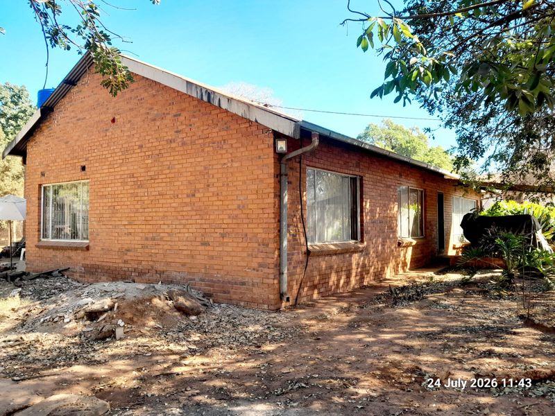 Rear view of a single-story brick farmhouse featuring exposed masonry walls, metal guttering, and aluminum-framed windows set within a natural garden area.