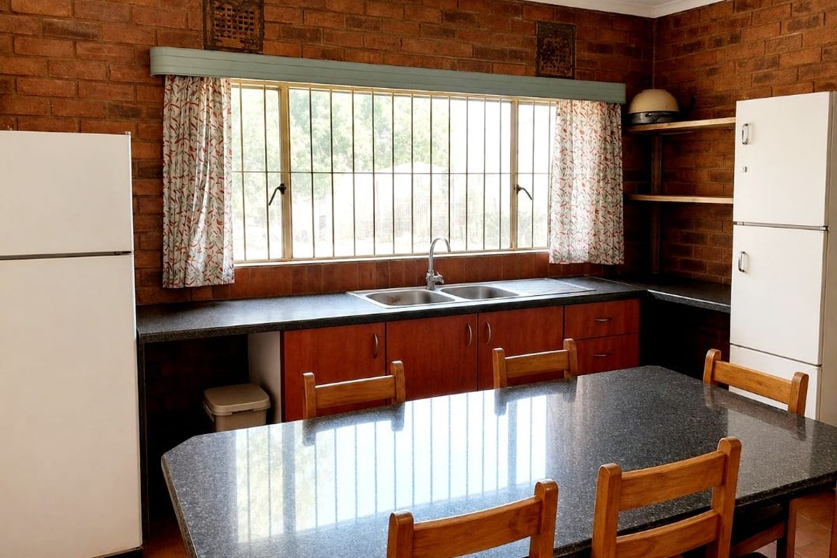 A rustic kitchen featuring exposed brick walls, built-in wooden cabinetry, laminate countertops, and a double bowl stainless steel sink.