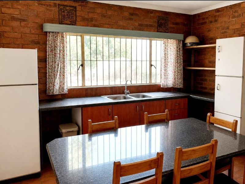 A rustic kitchen featuring exposed brick walls, built-in wooden cabinetry, laminate countertops, and a double bowl stainless steel sink.