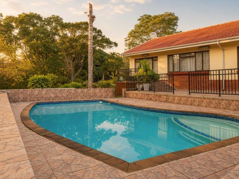 A well-maintained outdoor pool area featuring a tiled surround, metal safety balustrades, and a view of the rear garden and house elevation.