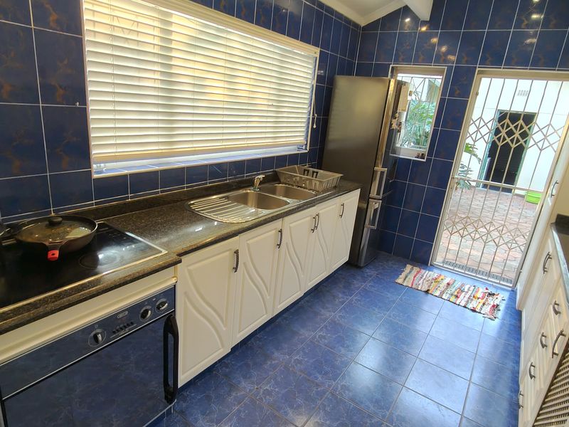 A functional kitchen featuring blue tiled walls and flooring, granite countertops, built-in cabinetry, and direct access to an outdoor area via a security gate.