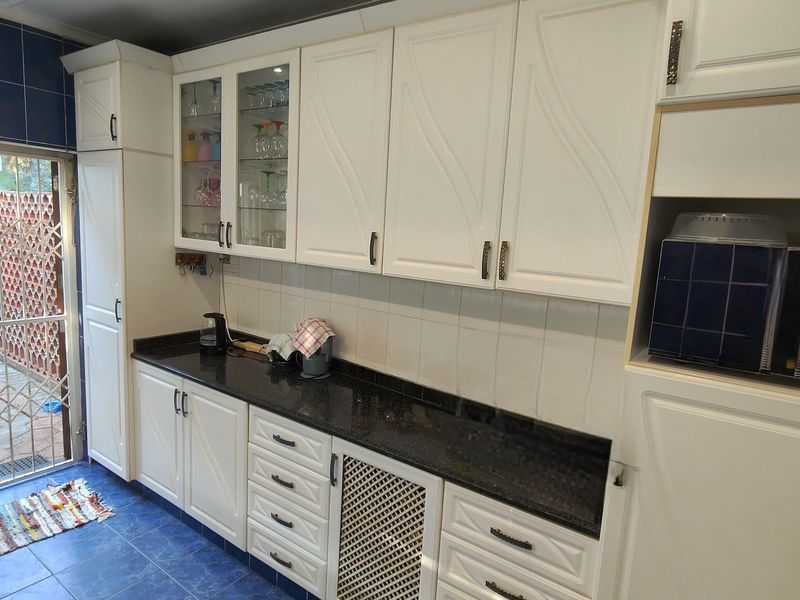 A functional kitchen featuring white cabinetry, black granite countertops, and blue tiled flooring, with direct access to an outdoor area through a security gate.