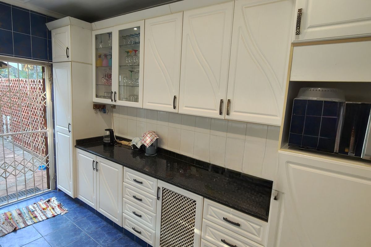 A functional kitchen featuring white cabinetry, black granite countertops, and blue tiled flooring, with direct access to an outdoor area through a security gate.