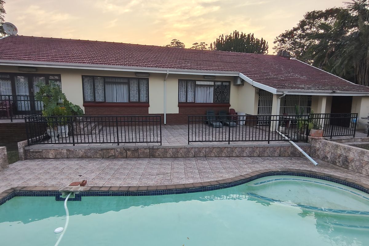 Rear exterior view featuring a tiled patio area, swimming pool, and a single-story house with a pitched roof and security railings.
