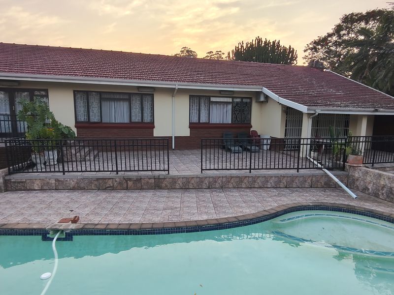 Rear exterior view featuring a tiled patio area, swimming pool, and a single-story house with a pitched roof and security railings.