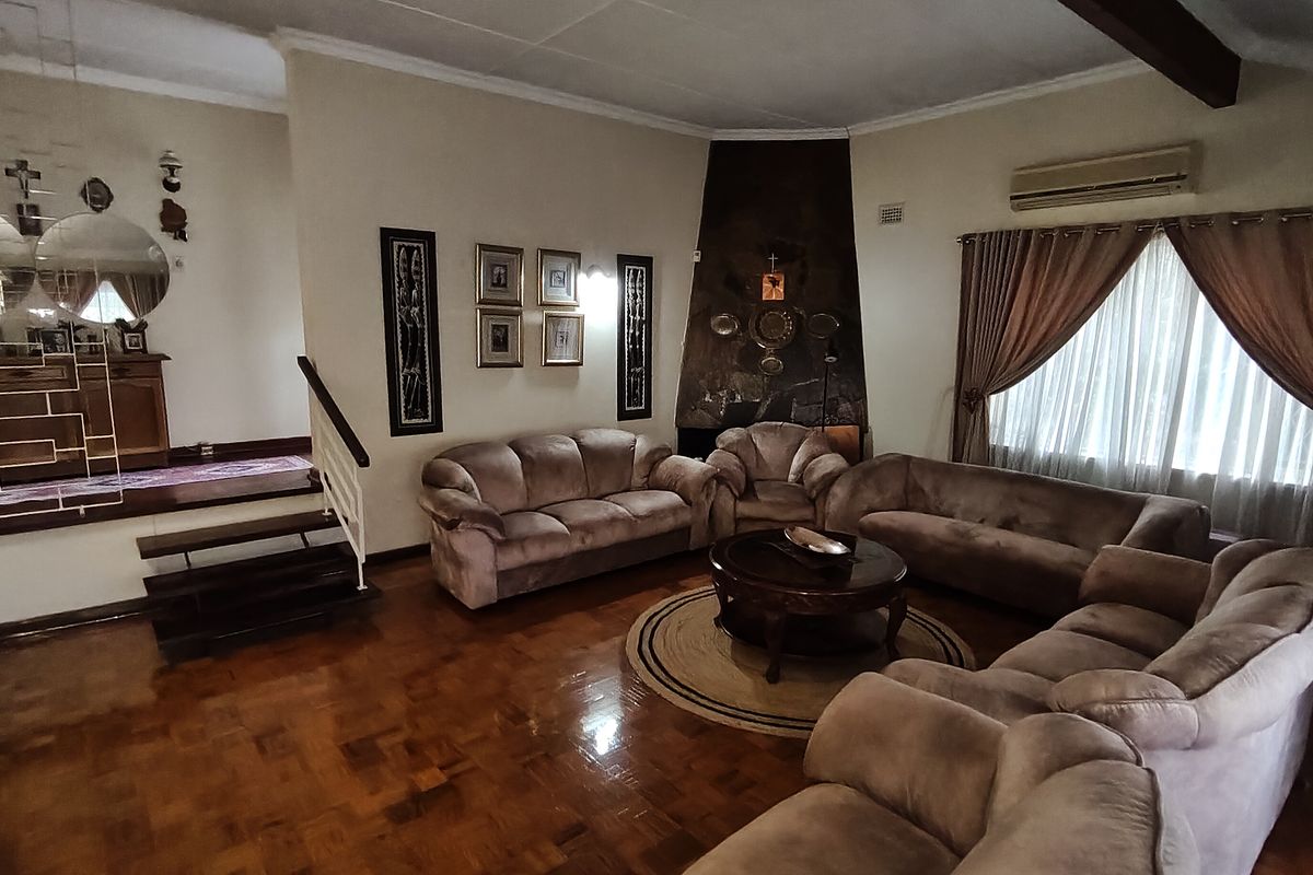 Spacious living room featuring polished parquet flooring, a prominent stone fireplace, and an integrated split-system air conditioner, with an adjacent staircase leading to another level.