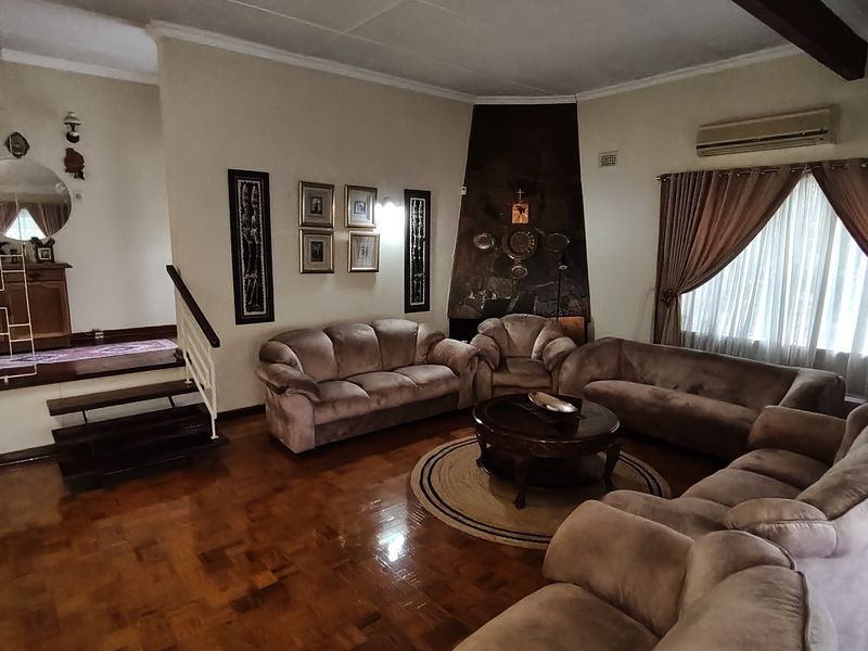 Spacious living room featuring polished parquet flooring, a prominent stone fireplace, and an integrated split-system air conditioner, with an adjacent staircase leading to another level.