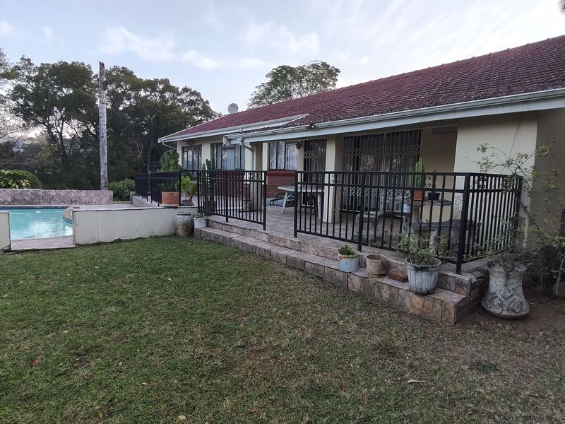 Rear view of the property featuring a tiled patio area, metal security railings, and an adjacent swimming pool set within a garden.