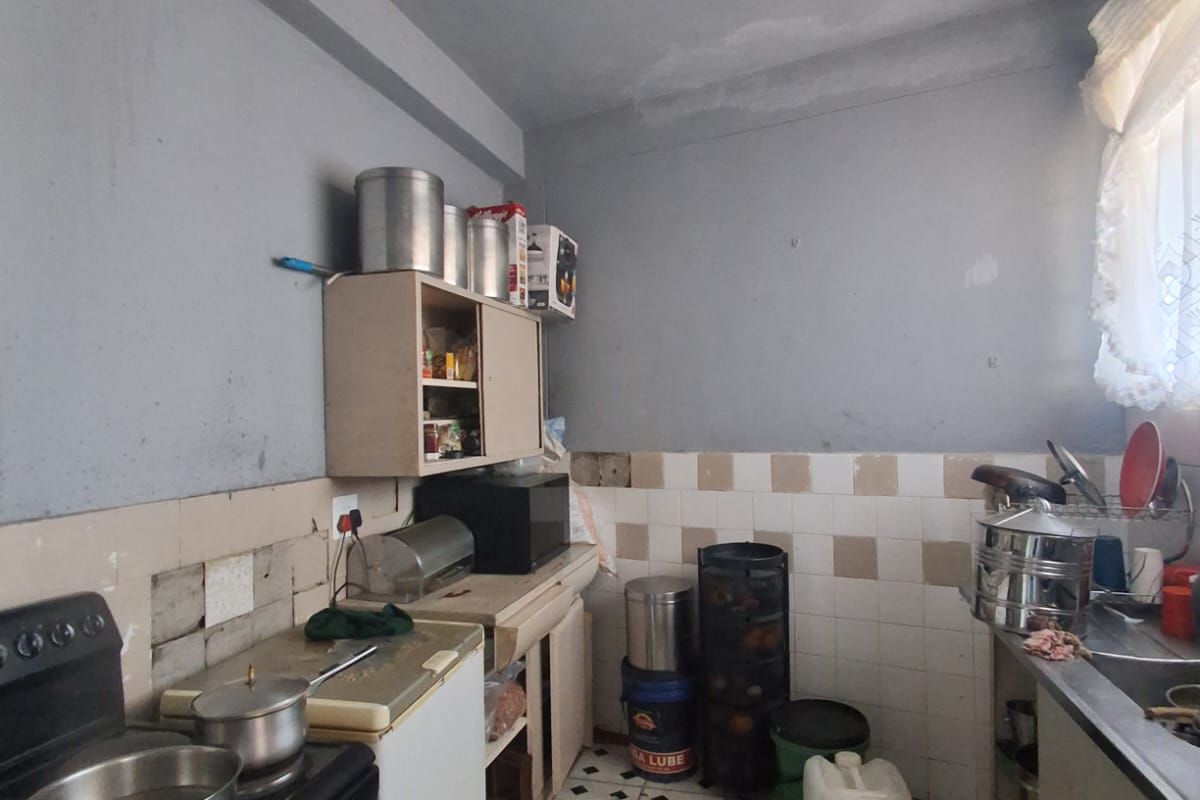 A dated kitchen featuring original cabinetry, tiled splashbacks, and a stainless steel sink, requiring significant renovation and cosmetic updates to modernize the space.