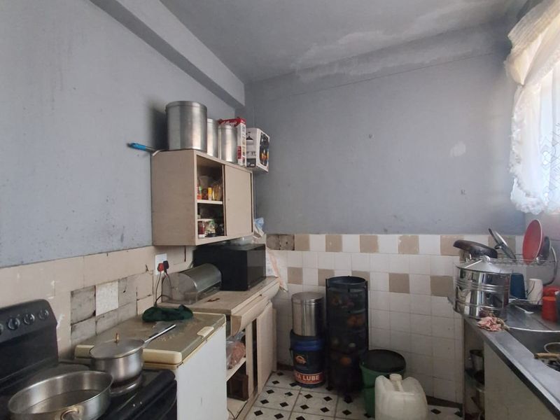 A dated kitchen featuring original cabinetry, tiled splashbacks, and a stainless steel sink, requiring significant renovation and cosmetic updates to modernize the space.