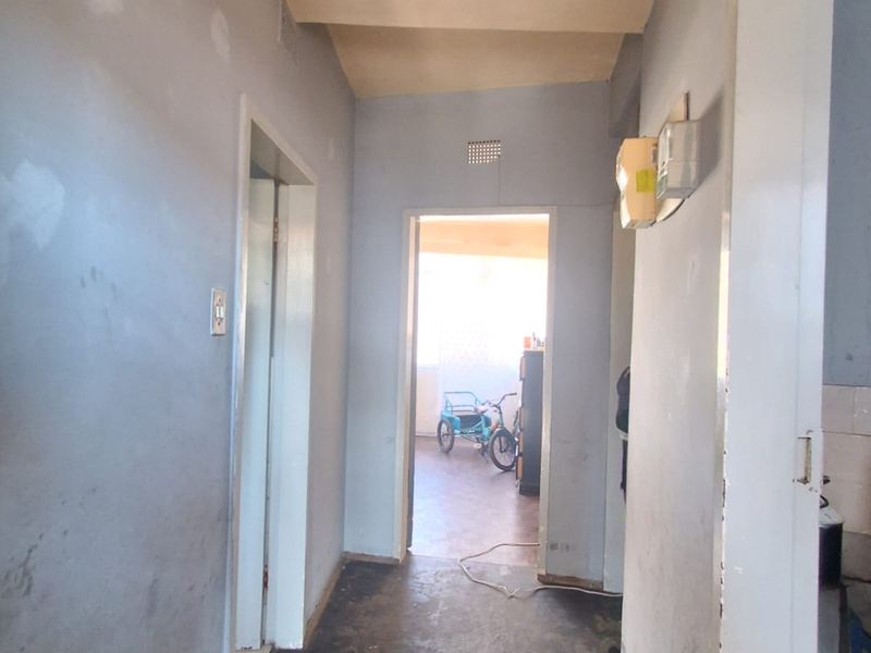 A narrow hallway with worn flooring and walls requiring cosmetic attention, leading towards an adjacent living space.