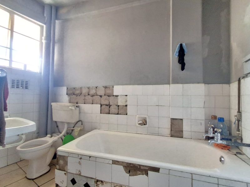 A bathroom in need of renovation, featuring a bathtub, toilet, and wall-mounted basin with significant tile damage and exposed wall surfaces.