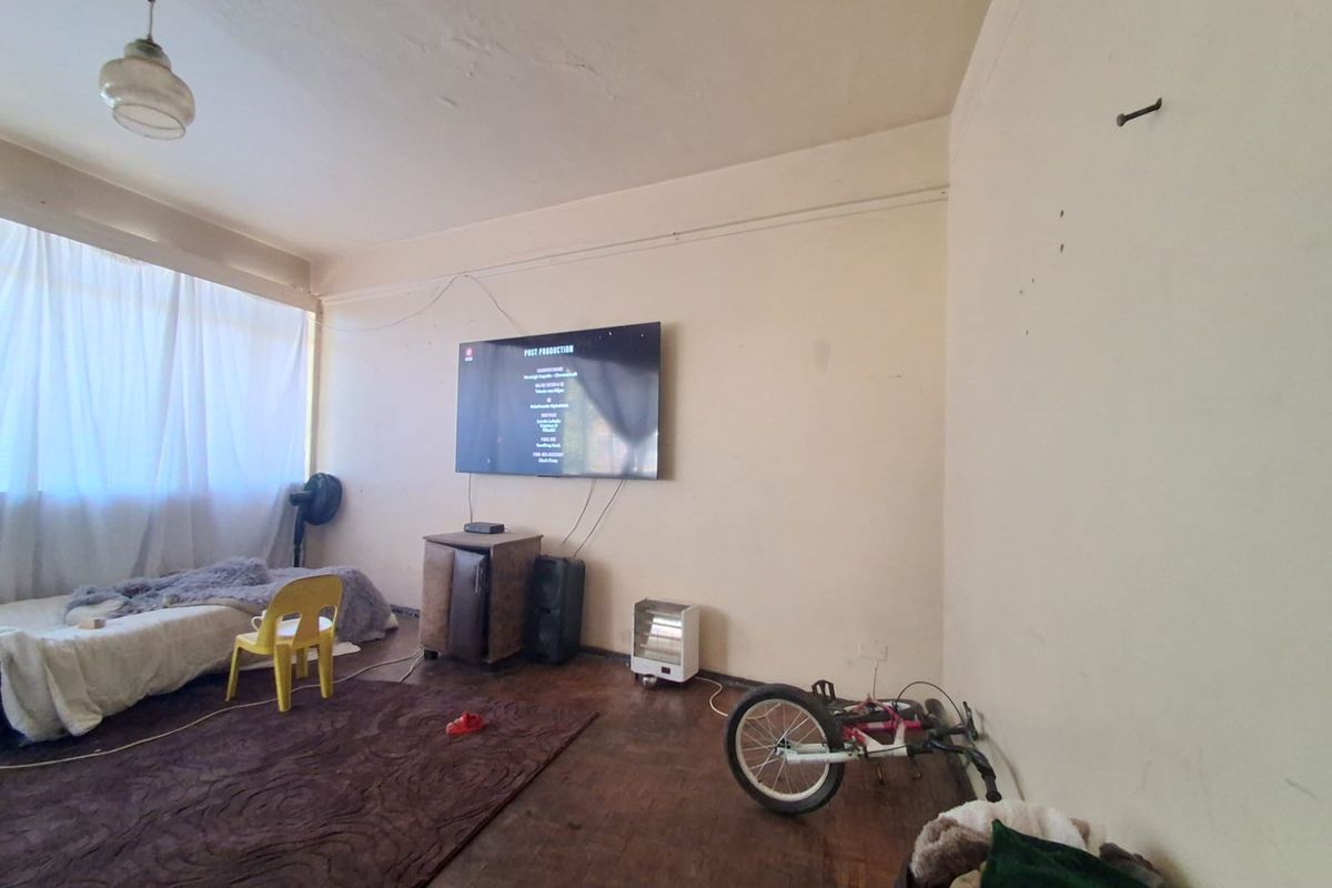 A living room featuring original parquet flooring and a wall-mounted television, requiring cosmetic updates to the walls and ceiling to improve the overall finish.
