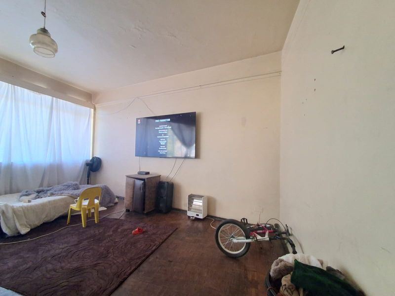 A living room featuring original parquet flooring and a wall-mounted television, requiring cosmetic updates to the walls and ceiling to improve the overall finish.