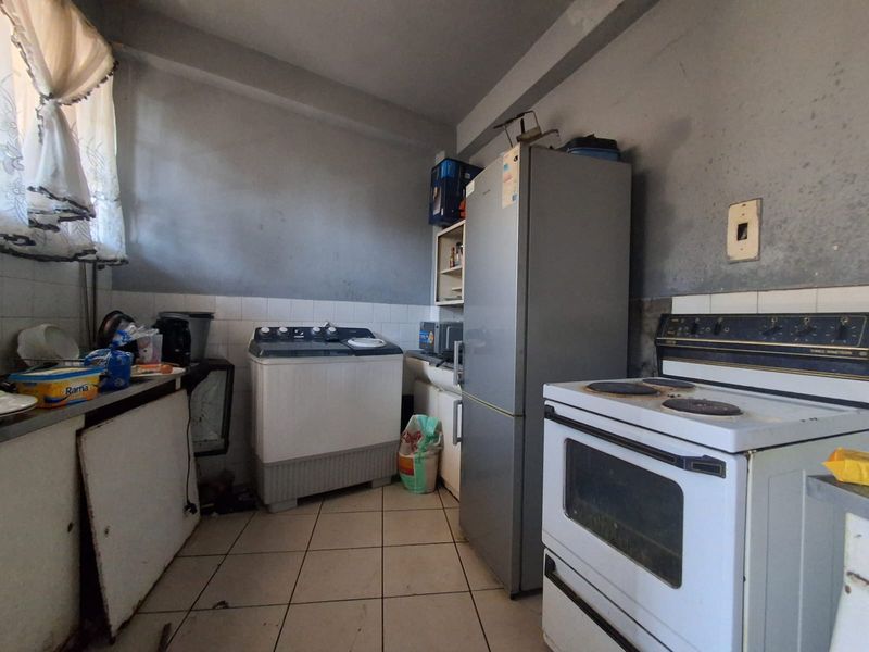 A functional kitchen space featuring tiled flooring, a built-in stove and oven, and tiled splashbacks, currently requiring cosmetic updates and maintenance.