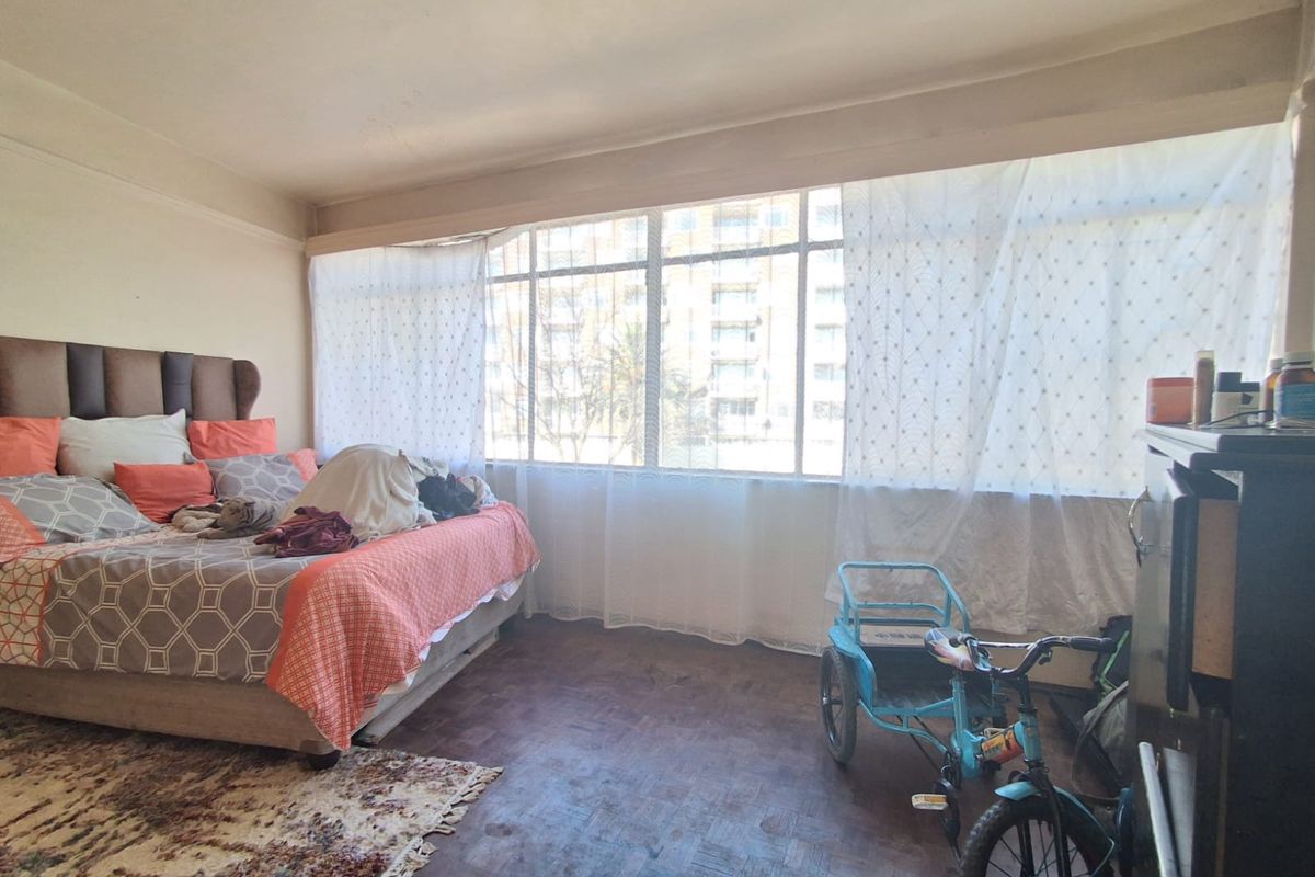 A spacious bedroom featuring original parquet flooring and a large window that provides ample natural light.