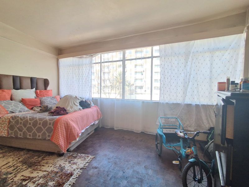 A spacious bedroom featuring original parquet flooring and a large window that provides ample natural light.
