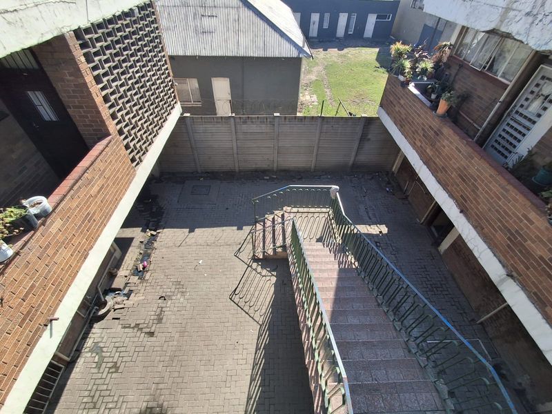 An elevated view of a paved rear courtyard area featuring a central metal staircase, brick building facades, and a perimeter boundary wall.