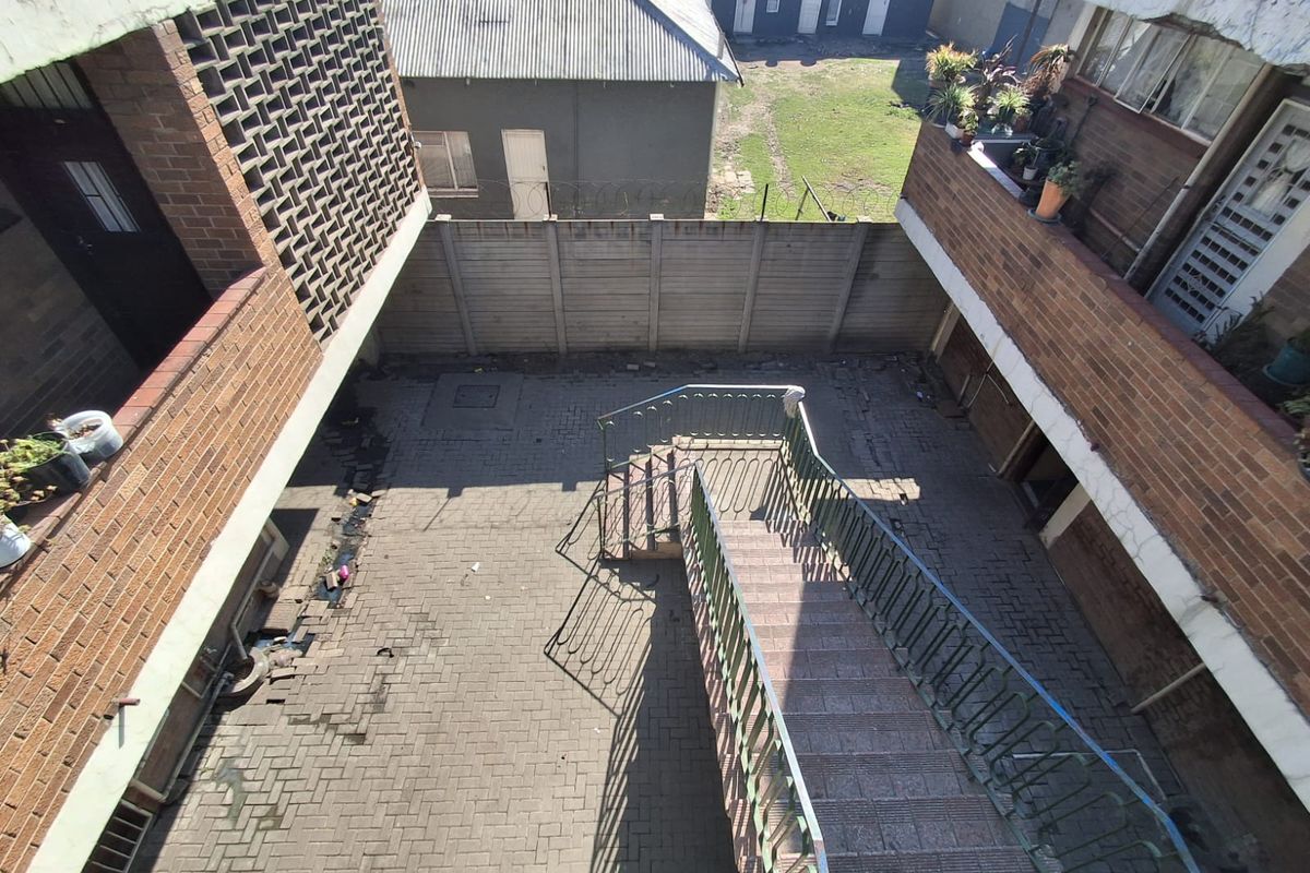 An elevated view of a paved rear courtyard area featuring a central metal staircase, brick building facades, and a perimeter boundary wall.