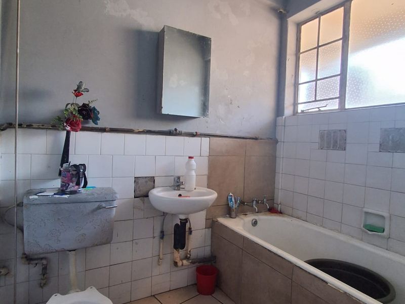 A dated bathroom featuring a bathtub, wall-mounted basin, and toilet, requiring significant renovation and cosmetic updates to improve its condition and functionality.