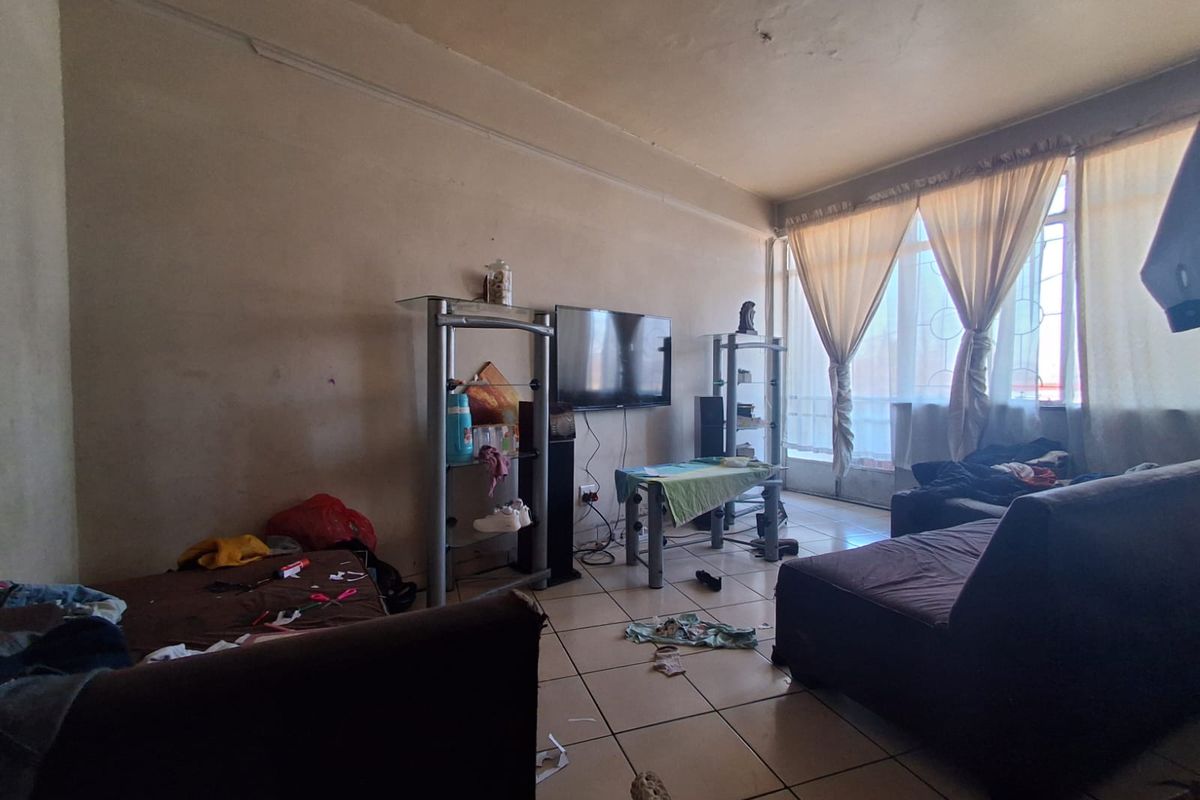 A living room area featuring tiled flooring and a large window, currently requiring cosmetic updates and wall repairs to improve the overall condition.