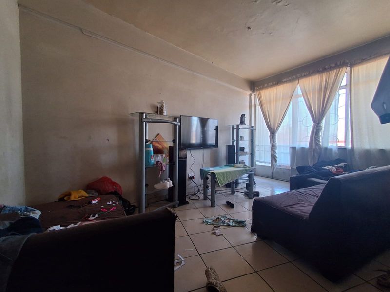 A living room area featuring tiled flooring and a large window, currently requiring cosmetic updates and wall repairs to improve the overall condition.