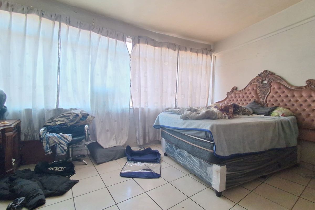 A bedroom featuring tiled flooring and a large window, currently requiring cosmetic updates to the wall finishes.