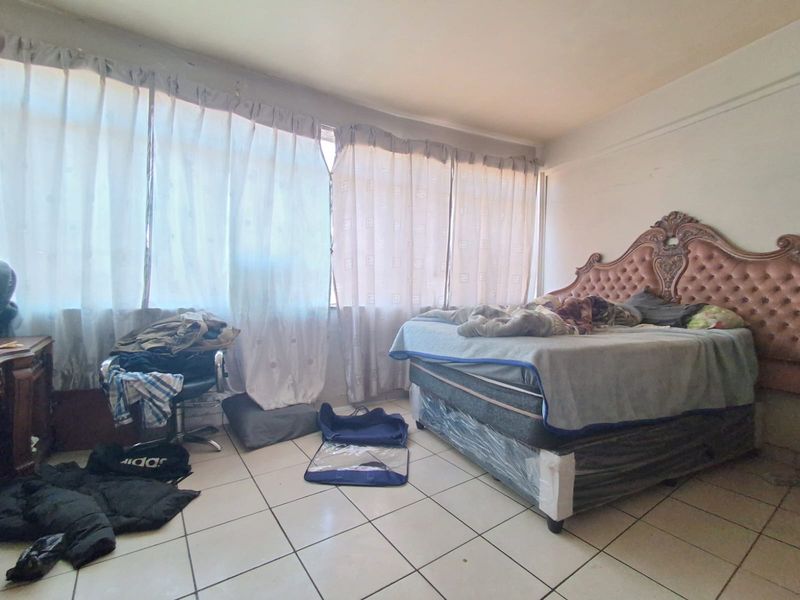 A bedroom featuring tiled flooring and a large window, currently requiring cosmetic updates to the wall finishes.