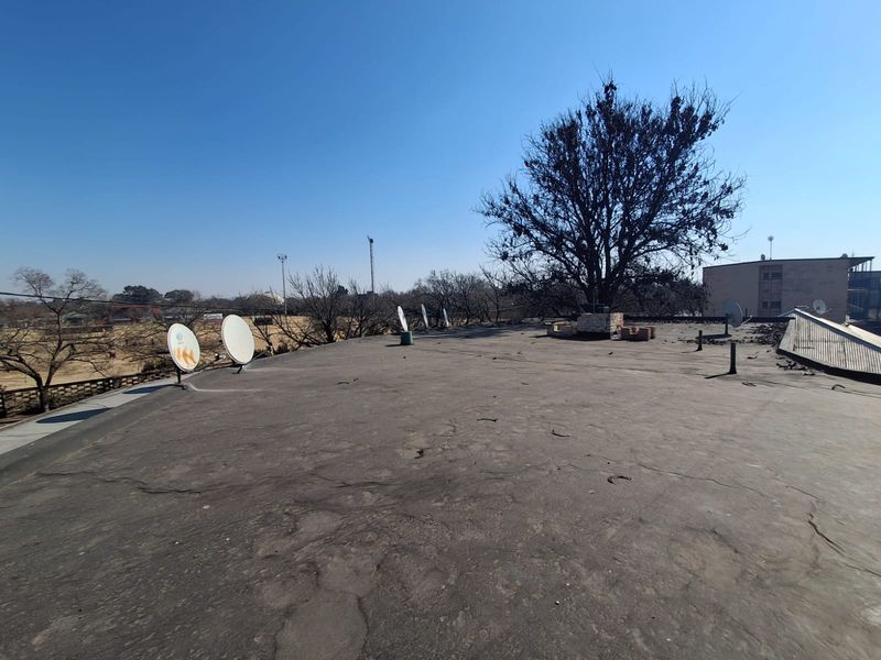An elevated view of a flat roof surface showing signs of wear and weathering, featuring multiple satellite dishes installed on the roof.