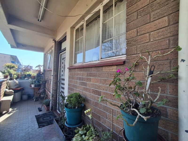 A covered balcony area featuring brick exterior walls, tiled flooring, and security gate access, offering potential for outdoor seating and relaxation.