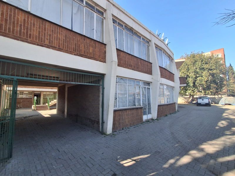 Exterior view of a multi-story apartment building featuring brick facade, concrete structural columns, and paved driveway access.