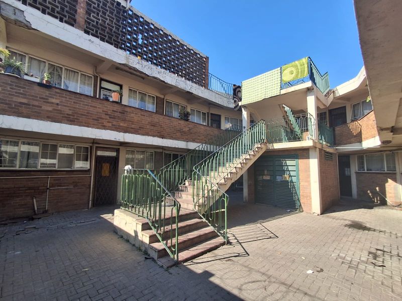 A view of the rear courtyard featuring a brick facade, external concrete staircase with metal railings, and paved ground area.