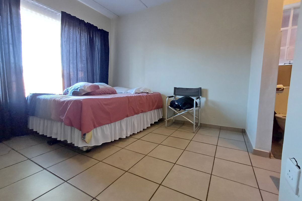 A simple bedroom featuring tiled flooring and a large window, with an adjacent view into a bathroom area.