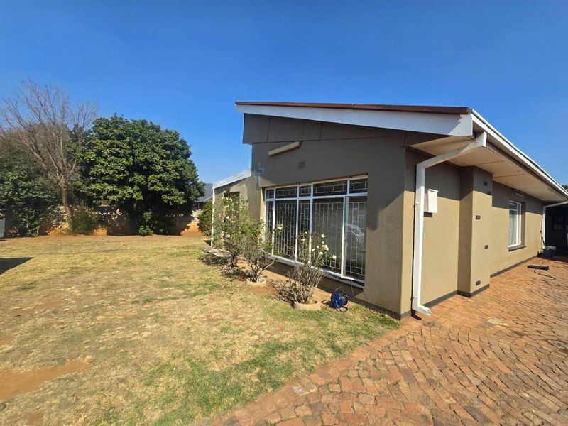 Rear view of the property featuring a brick paved driveway, security bars on windows, and a large garden area.