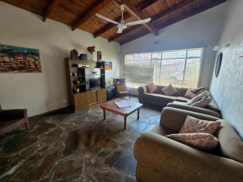 Spacious living room featuring a high exposed timber beam ceiling, unique flagstone flooring, and a large window providing ample natural light.