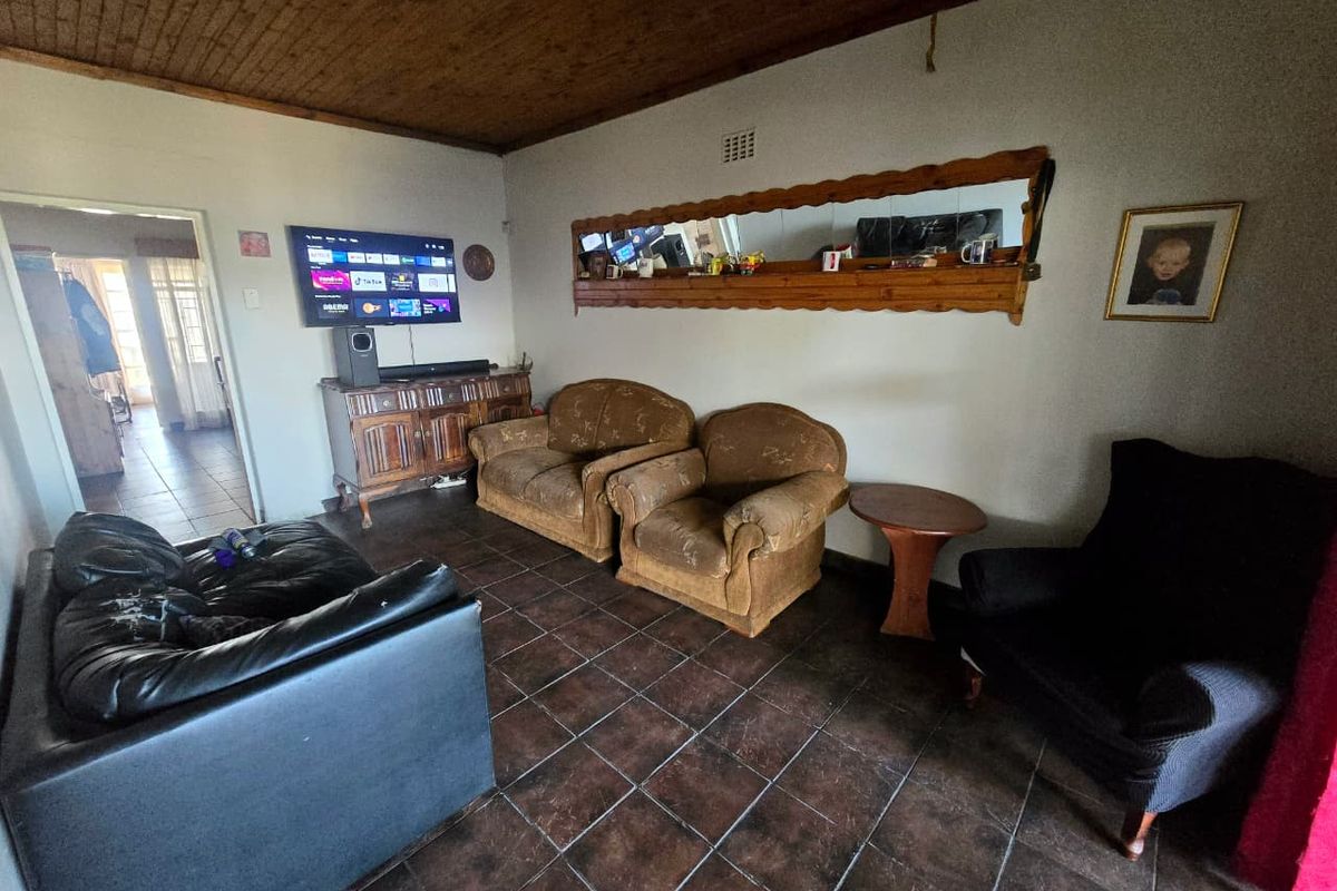 A living room featuring dark tiled flooring and a timber-paneled ceiling, offering a dated aesthetic that could be modernized with updated finishes.