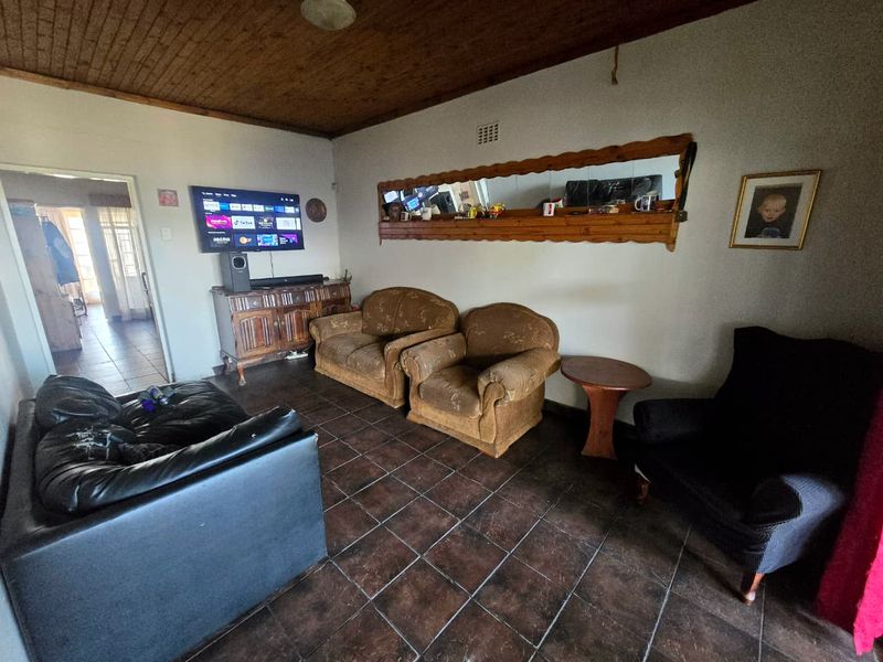 A living room featuring dark tiled flooring and a timber-paneled ceiling, offering a dated aesthetic that could be modernized with updated finishes.